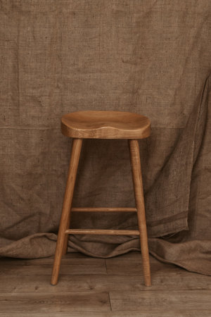Single Tall Wooden Leg Stool on brown textile background