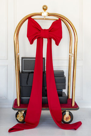 Golden luggage cart with black gift boxes and big red bowの写真素材