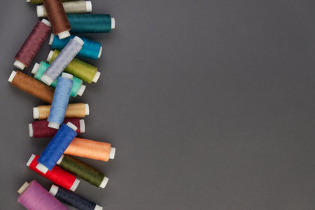 Colored sewing threads are laid out on a gray background, space for text.