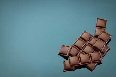Broken dark chocolate bar on a blue background, space for text.の写真素材