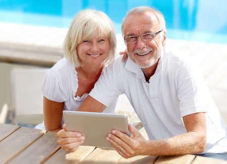 Different aged couple using a Tablet PC outside on the pool Different aged couple using a Tablet PC outside on the pool