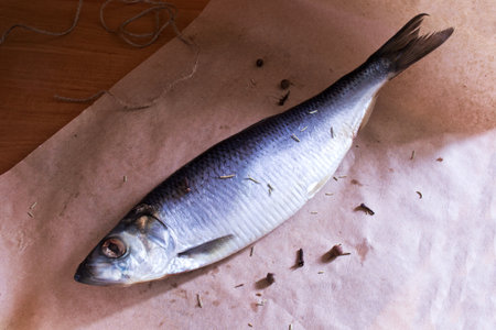 Salted herring with spices in a wrapping paper on wooden tableの写真素材