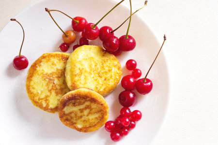 Frying homemade cottage cheese pancakes syrniki with cherry and red currant on a plateの写真素材