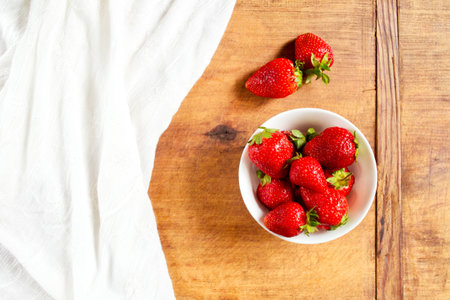 Fresh and ripe strawberries in a bowl on a wooden tableの写真素材