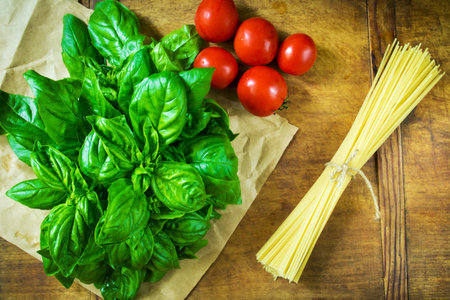 Fresh green basil, tomatoes and pasta before cooking on a wooden tableの写真素材