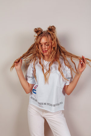 Pretty smiling young European girl keeps eyes closed with pleasure, feels comfortable and fulfilled. Wavy surf hair. Girl wearing white t-short  isolated on beige background.の写真素材
