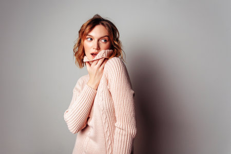 Pretty surprised young european. Wavy surf hair. Girl wearing pink sweater, isolated on gray background.の写真素材