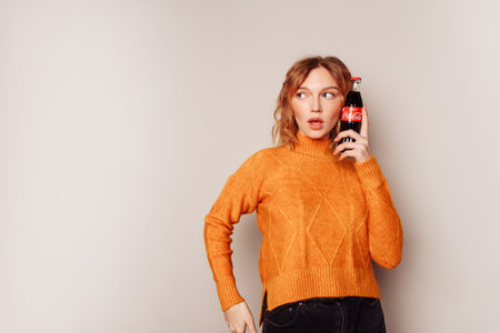 Pretty surprised young european girl with bottle of coca-cola in her hand.  Wavy surf hair. Girl...