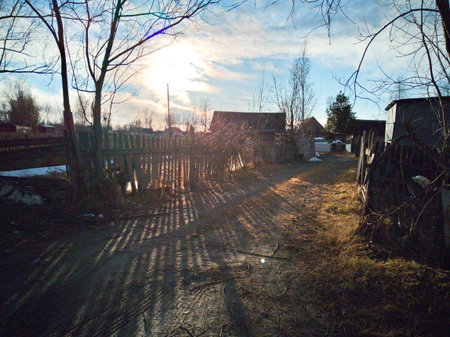 Sunset in a small village in the winter. The sun shines through the trees.の写真素材