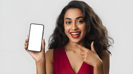 Smiling woman pointing at blank smartphone screen, promoting mobile app, mockup, or digital product in studio with copy space.の素材
