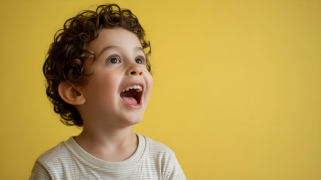 Joyful curly-haired child smiling with excitement on yellow background, expressing happiness, innocence, and childhood emotions in a vibrant studio portrait.の素材