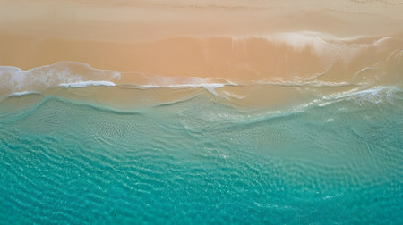Aerial view of turquoise ocean waves gently washing onto a sandy beach, showcasing tropical paradise, relaxation, and natural beauty.の素材