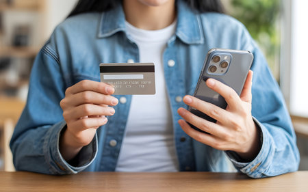 Woman holding a credit card and smartphone, engaged in secure online shopping and mobile banking.の素材