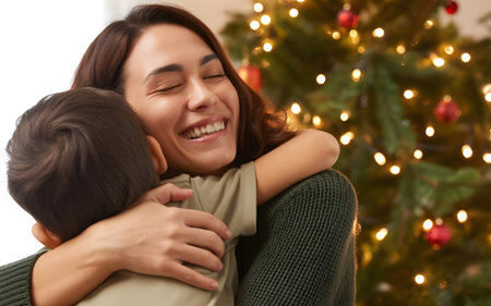 Joyful mother hugging child in front of glowing Christmas tree. Warm family holiday moment.の素材