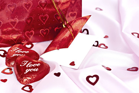 Pink bedding, gift box with a blank card, chocolates with the words I Love You and a lot of small distributed hearts. Surprise to the woman.の写真素材