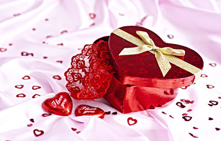Pink bedding, gift box heart-shaped chocolate candy with the words I Love You and a lot of small distributed hearts. Surprise to the woman.の写真素材