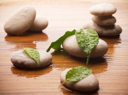 Massage stones with green leaves and water drops. Wood background.の写真素材