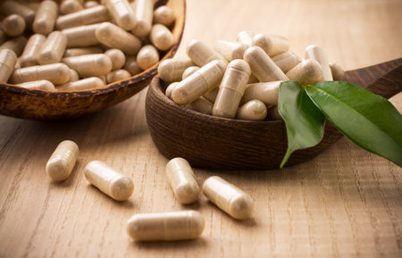 Alternative medicine tablets on a wooden spoon, green leaf.の写真素材