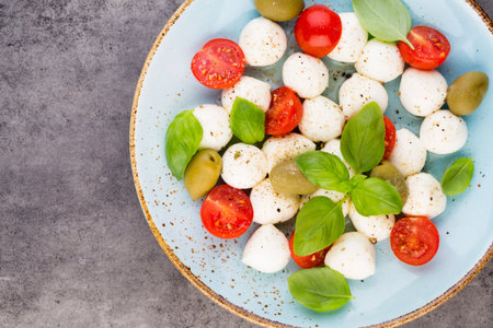 Cherry tomatoes, mozzarella cheese, basil and spices on gray slate stone chalkboard. Italian traditional caprese salad ingredients. Mediterranean food.の写真素材