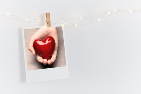 The polaroids photo red heart pinned on a lantern, white wall background.の写真素材