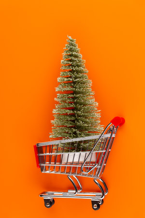 Shopping cart with christmas tree on red table.の写真素材