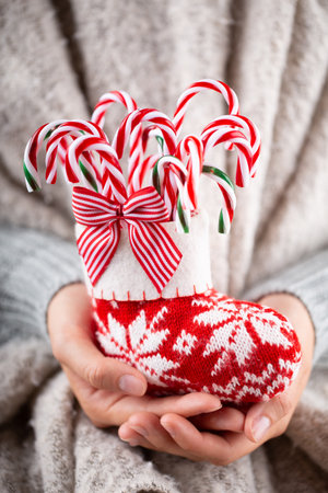 Winter Concept Young Hands Holding christmas candy canes, stick decor.  Christmas decoration idea. Christmas canes, stick in the hands of a woman, background with gold bokeh.の写真素材