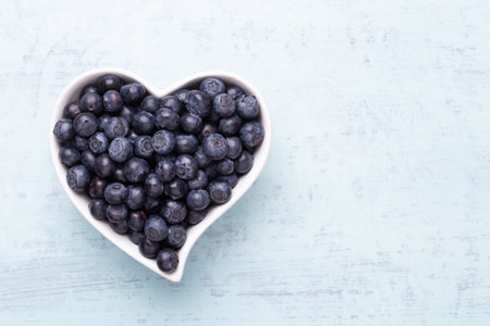 Fresh blueberries, in a heart shaped bowl on a wooden background.の写真素材