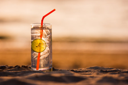 Picture of a glass of Gin Tonic with straw and lime slice on the beach, at sunset. Long Beach, Ko Lanta, Thailand.の写真素材