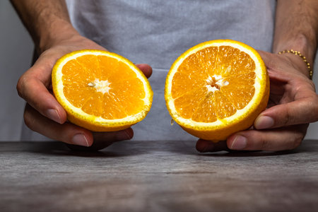Male hands cutting a ripe orange with a knife on a slate table. front view.の写真素材