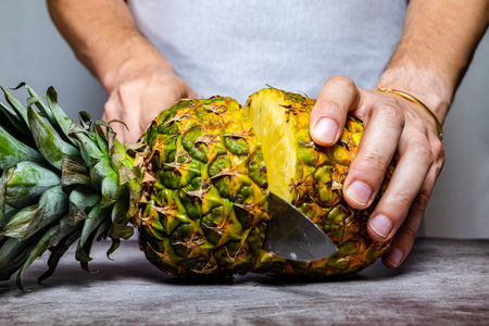 Male hands cutting a ripe Pineapple with a knife on a slate table. front view.の写真素材