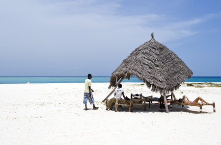 Zanzibar, Tanzania - February 27, 2008: Northern coast, local young servant and a tourist on the  beachのeditorial素材
