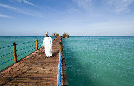Zanzibar, Tanzania - February 28, 2008: A servant on the wharf with bungalows of an holiday village on the eastern coastのeditorial素材