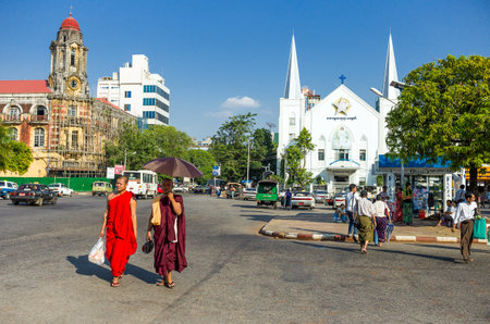 Yangon,  Myanmar - January 9, 2012:  Two monks in a square of the city center with a Baptist church in the background.のeditorial素材