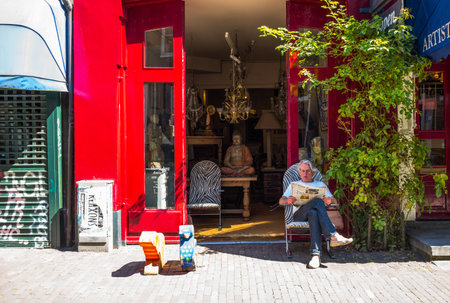 Amsterdam, Holland - July 23, 2014:  A man sitting in front of an art shops in Spiegelkwartierのeditorial素材