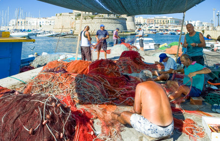 Gallipoli, Italy - August 28, 2006: Fishermen working on the nets in the harbor with the Rivellino fortress (XVI century) in the backgroundのeditorial素材