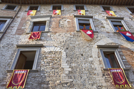 Italy,Umbria,Gubbio, Dei Consoli street, the  facade of a medieval house with gonfalons of the districts of the townの写真素材