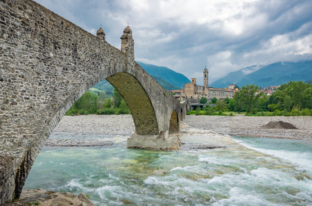 Bobbio, Italy, the Old Bridge (also known as the Devil's Bridge) over the Trebbia river, with the country in the backgroundの写真素材