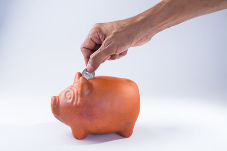hand putting coin into a piggy bank on a white background.