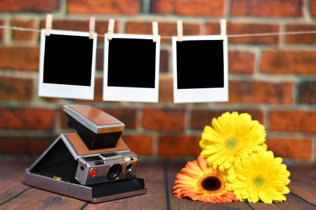vintage camera with yellow and pink daisies on wood slats, snapshots photographs hanging with brown bricks backgroundの写真素材