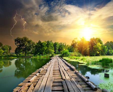 Lightning over a wooden bridge on a riverの写真素材