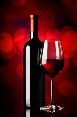 Bottle and glass with red wine on red backgroundの写真素材