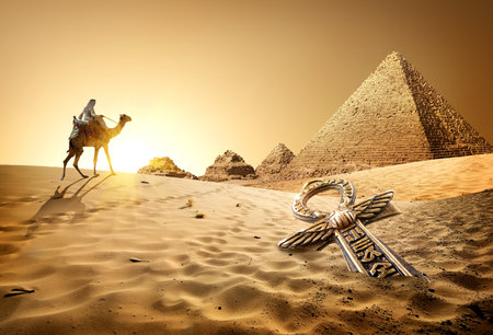 Bedouin on camel near pyramids and ankh in desert