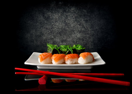 Sushi on plate with red chopsticks on black backgroundの写真素材