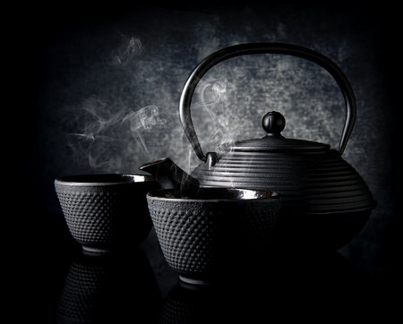 Black teapot with small cups on black backgroundの写真素材