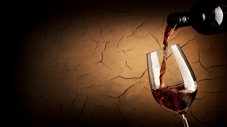 Wine pouring in wineglass in cellar with clay wallの写真素材
