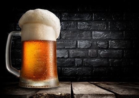 Mug of beer on table near black brick wallの写真素材