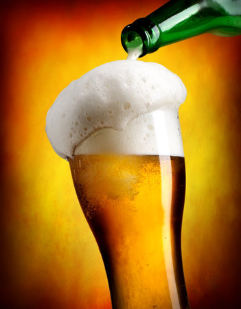 Beer pouring from bottle in tumbler on orange backgroundの写真素材