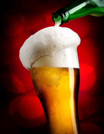 Beer pouring from bottle into glass on red backgroundの写真素材