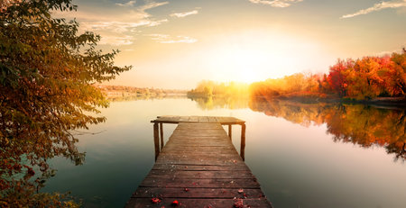 Red autumn and wooden fishing pier on riverの写真素材