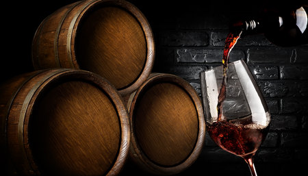 Wooden barrels and wine pouring into wineglass in cellarの写真素材